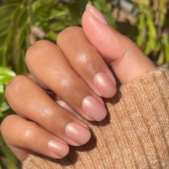 Hand with oval nails polished in shimmery Cookie Swap gel polish against a soft natural outdoor background