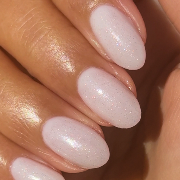The Celestial Effect Top Coat on natural nails with a soft white base and fine shimmering micro-shimmer for a radiant mani